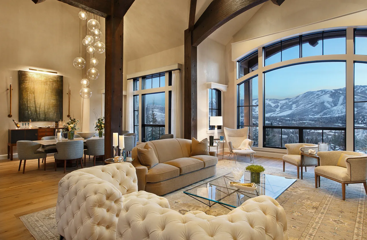 Great room with a vaulted timber-trussed ceiling, two cream tufted sofas and a wall of arched windows looking out to snowy mountains