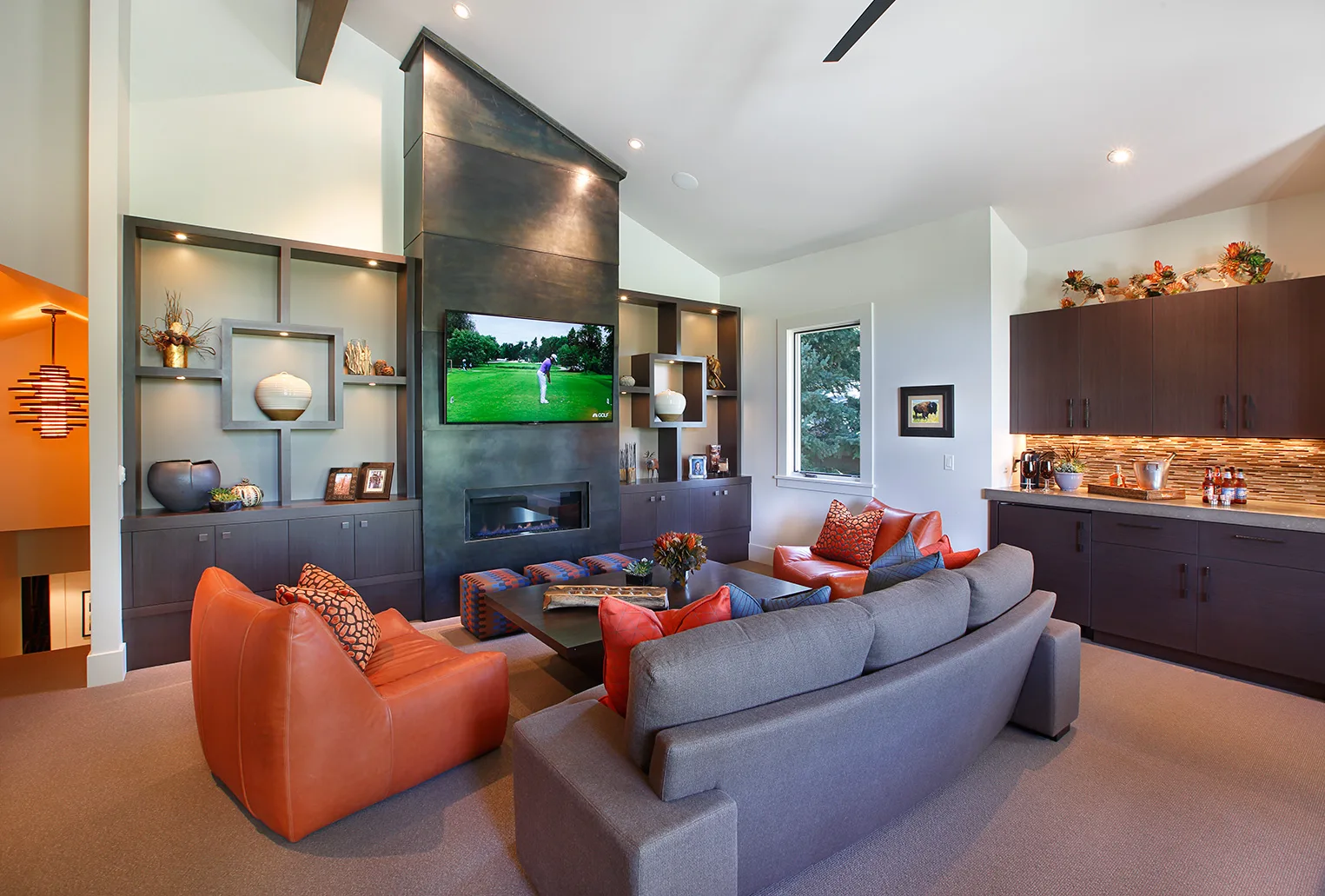Modern living room with orange leather chairs, a gray sofa and a fireplace wall with a mounted TV and built-ins