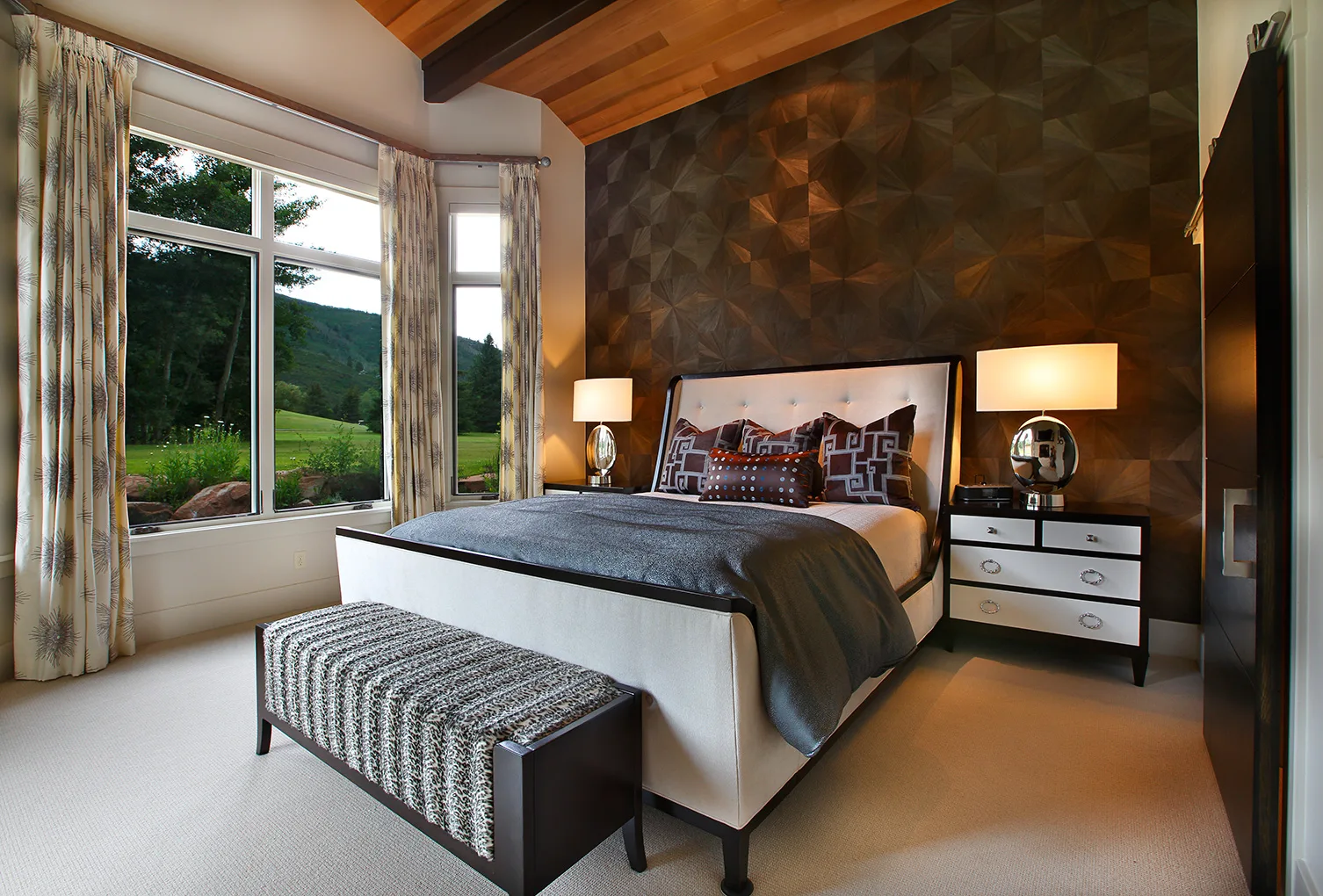 Bedroom with a window seat bench, nightstand lamps and a mountain view through the window