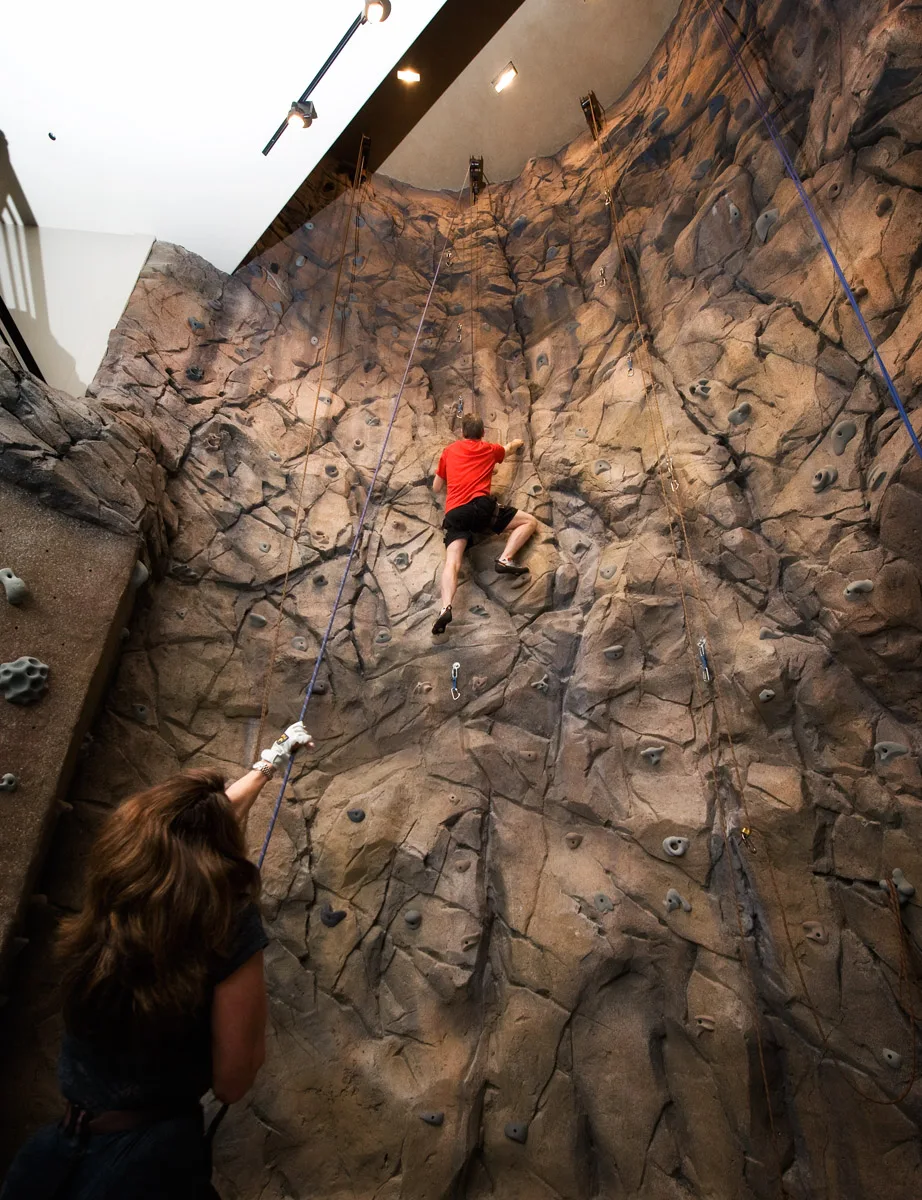 Indoor rock climbing wall with a person climbing, belayed from below