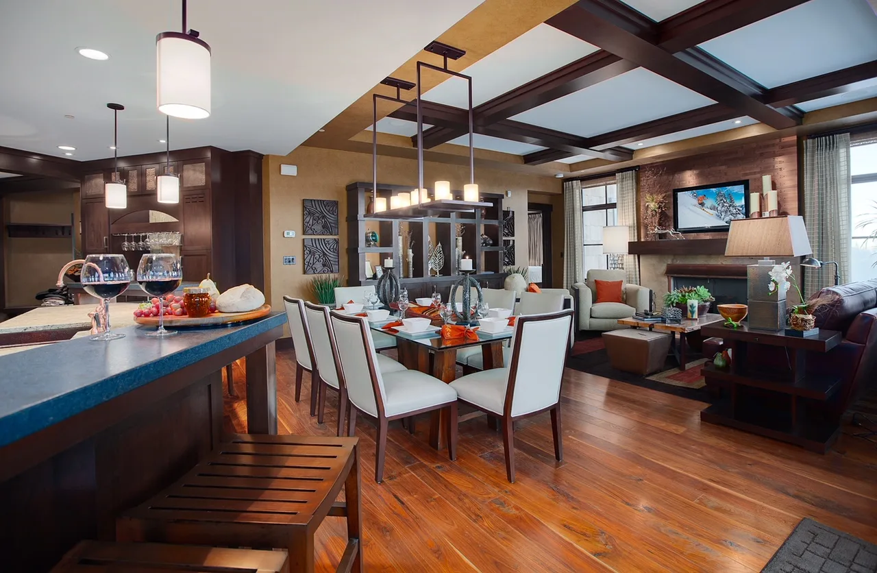 Open-plan living and dining room with a coffered ceiling, fireplace, a table set for dinner and a mounted TV