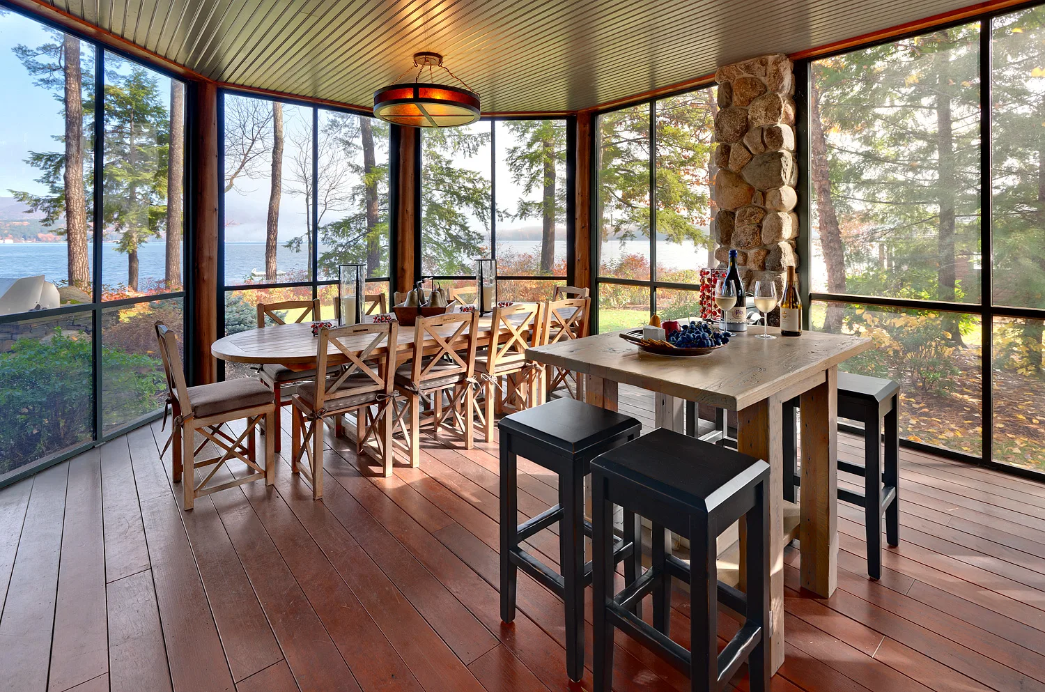 Screened porch with a dining table and chairs, wood floors and a lake view through the screens