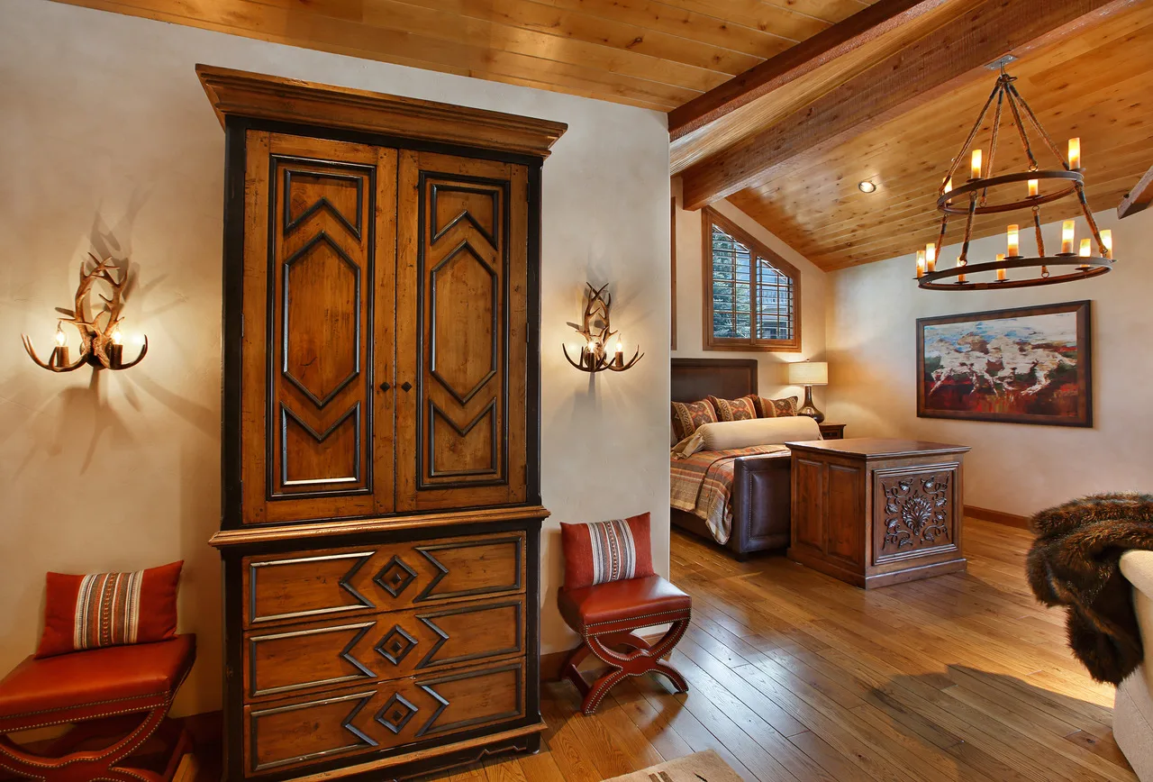Bedroom with a carved wood armoire, chandelier and antler wall sconces